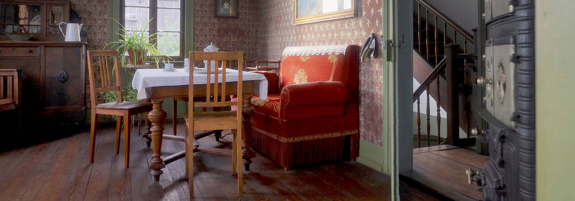 Innenansicht einer Stube aus dem 19. Jahrhundert mit Esstisch, zwei Stühlen und einer Sitzbank