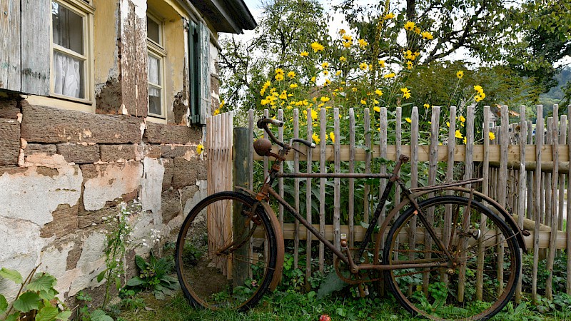 Altes rostiges Fahrrad lehnt an einem Zaun neben einem historischen Gebäude