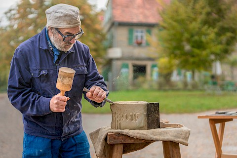 Ein Steinmetz bearbeitet mit seinem Werkzeug einen Steinquader
