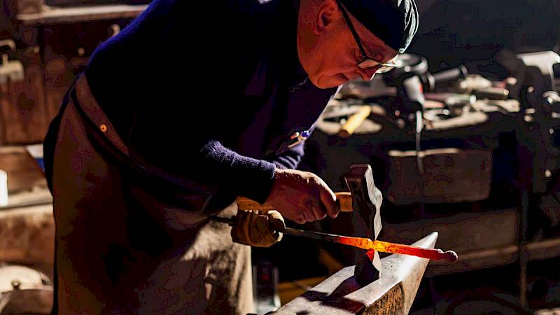 Ein Schmied bearbeitet ein glühendes Eisen in einer alten Schmiedewerkstatt